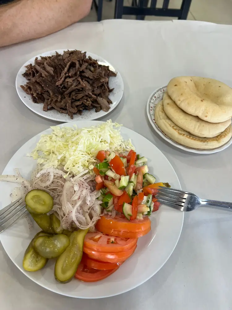 צלחת שווארמה לצד פיתות וצלחת סלטים.